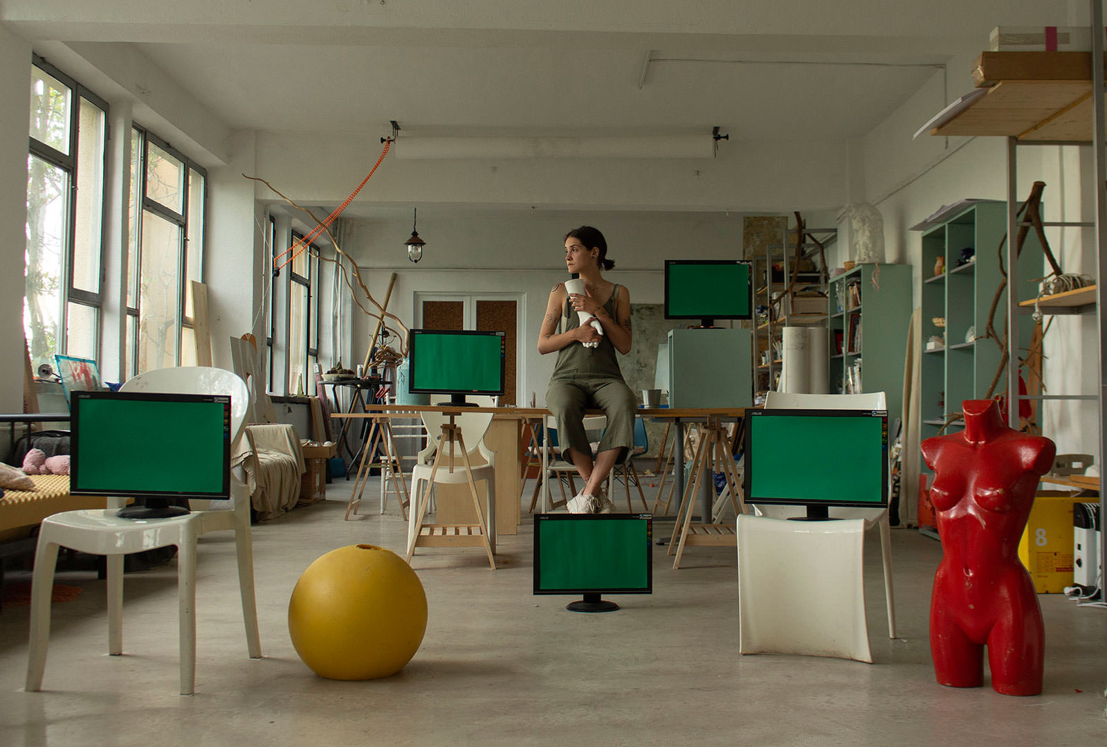 Atelierinnenraum mit sitzender Frau und mehreren Bildschirmen