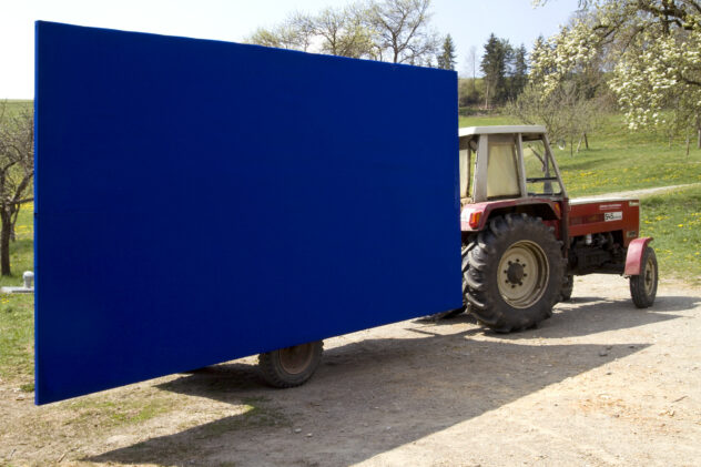 Traktor zieht einen Anhänger mit einem großen monochromen blauen Bild